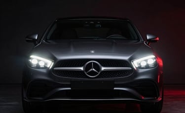 Low-angle photography of a luxury European car in a dark, minimalist studio in Southeast Asia. The sharp LED headlamps are glowing with a crisp white light, reflecting on the polished floor. Minimalist composition with deep black shadows and subtle red lighting accents. Professional automotive photography style.