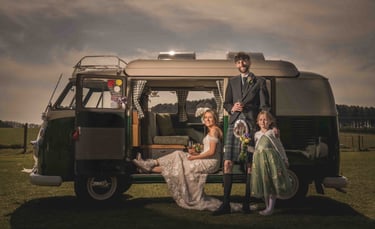 Scottish wedding couple in a kilt and lace gown posing with a child by a vintage VW camper van.