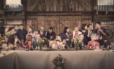 Wedding party celebration at a rustic barn reception with guests toasting at a long table.