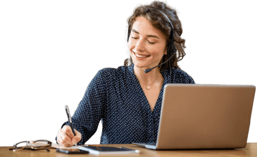 Smiling female customer service agent with headset taking notes while working on a laptop.