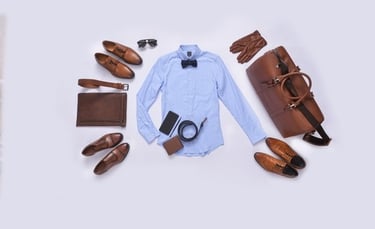 Flat lay of men's formal fashion accessories including a blue shirt, brown leather shoes, and a duffel bag.