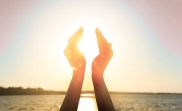 Deux mains levées encadrant le soleil au bord de l’eau