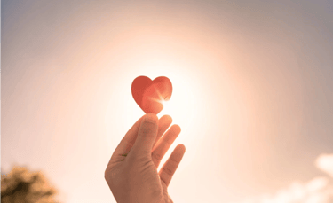 Une personne montre un cœur rouge devant le soleil, symbolisant l'amour authentique rayonnant.