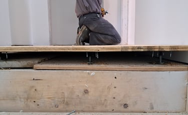 Contractor installing raised plywood subfloor using adjustable pedestals during residential floor levelling project