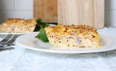Slice of baked macaroni and cheese casserole with ham and breadcrumb topping on a white plate.