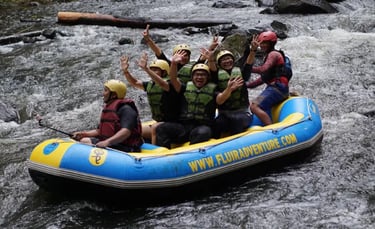 Sekelompok orang ceria sedang melakukan arung jeram di sungai berjeram, mengenakan helm kuning dan jaket pelampung, sambil me
