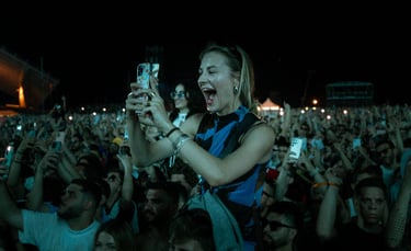 Excited woman on someone's shoulders, filming a concert. Energetic crowd with phones raised in the dark. Live music atmospher