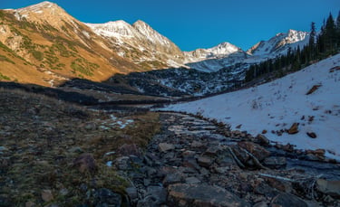 Beautiful snow-dressed high mountain peaks shine above Rustlers Gulch during fall sunset