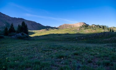 Wildflowers fill a lush basin below West Maroon Pass as sunrise highlights distant mountain peaks 