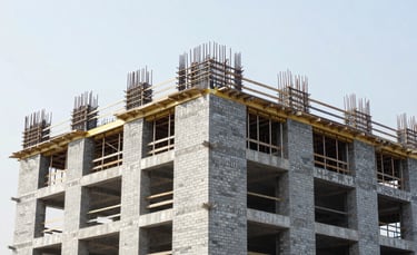 A wide angle shot of a modern South Asian construction site with clean masonry and precision scaffolding. The sky is bright, and the building structure shows high quality brickwork in a silver and blue grey tone.