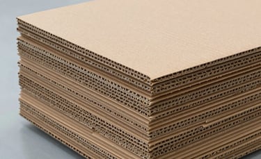 A close-up photograph of high-quality brown corrugated cardboard sheets stacked neatly in a modern industrial factory in Kuwait. The lighting is bright and clean, emphasizing the structural ridges of the cardboard against a professional white and slate blue background.