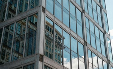 A close-up of a modern glass and steel building reflecting a clear blue sky in the US, symbolizing transparency, authority, and professional excellence.