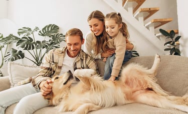 Happy family with a young daughter petting their golden retriever dog on a living room sofa.