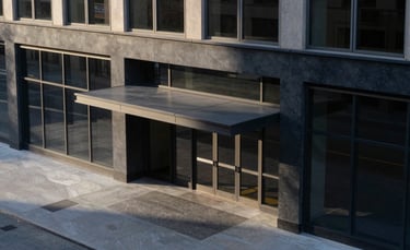 A minimalist, high-angle architectural photograph of a modern Chicago commercial building entrance with clean lines and large glass windows. The lighting is soft morning sunlight, casting subtle shadows. The color palette features deep navy and slate grey tones, projecting a sophisticated North American business vibe.