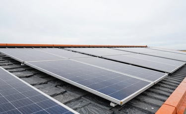 Wide angle view of clean, shiny solar panels on a modern roof reflecting a soft grey sky, high-contrast slate and orange tones
