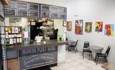 Interior of North Port Subs sandwich shop featuring a service counter, menu board, and local art.