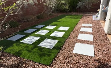Backyard with a checkered pattern of synthetic grass and decorative rocks, showcasing a clean.