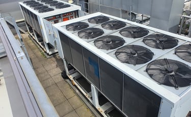 Large industrial HVAC chiller units with exhaust fans installed on a commercial building rooftop.