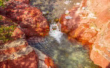 Clear water flowing through red rock formations at Red Rock Canyon in Waterton Lakes National Park.