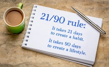 Notebook showing 21/90 rule for habit formation and lifestyle change with coffee and pen.