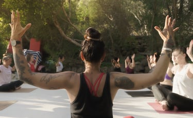 A group of women practicing yoga outdoors during a sunset retreat with their arms raised in cactus pose.