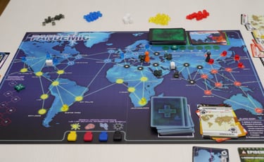 Stalo žaidimo lenta ant kurios sudėtos kortos, ligų kubeliai ir žaidėjų vaikštukai