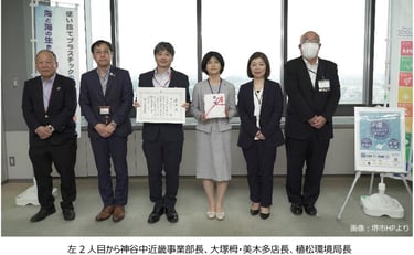 堺市役所で感謝状を受け取るダイエー関係者と堺市職員の集合写真。中央で感謝状と目録を持ち、プラスチック削減やSDGsの掲示が背景に写る。