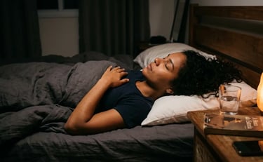 A woman with curly hair sleeping peacefully in bed with a glowing salt lamp on the nightstand.