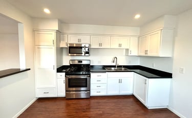 A modern kitchen with white cabinetry, black countertops, and stainless steel appliances