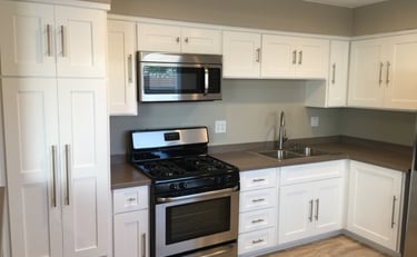 A modern kitchen with white cabinetry, grey countertops, and stainless steel appliances