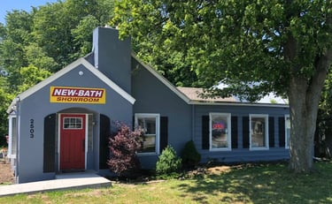 Front view of the New Bath Elite showroom in Perrysburg, Ohio, featuring a gray building with a red door, bright yellow logo 