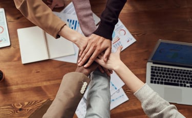 Handen van teamleden boven werktafel, symboliseert samenwerking en gezamenlijke verantwoordelijkheid