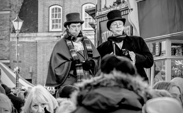 Performers in Victorian costumes with top hats and capes at a Dickensian Christmas festival.