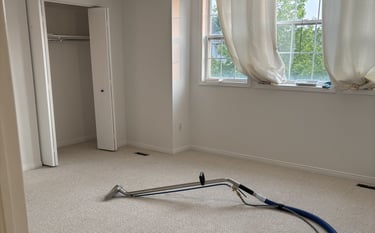 Professional carpet cleaning in an empty bedroom using a steam extraction wand and vacuum hose.