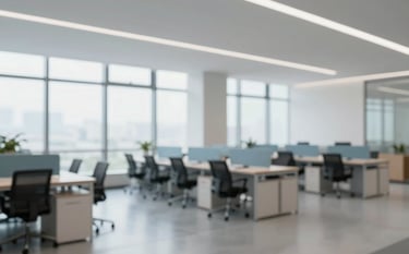 A wide-angle interior shot of a modern, clean office space with large windows and polished floors. The atmosphere is professional, hygienic, and bright, with subtle blue accents in the furniture.