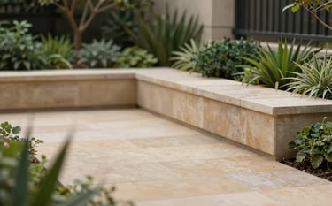 A sophisticated garden design featuring a modern stone terrace in tan tones (#C1A78B) and architectural plantings with dark green foliage (#2A3F30). The composition is balanced and inviting, showcasing professional landscape architecture and natural elegance.
