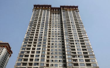 A high-rise modern residential complex under construction in a major Indian city like Mumbai or Bangalore. The photo is taken from a low angle, emphasizing scale and urban development. Professional architectural photography. South Asian / Indian.