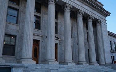 Photography of an elegant North American judicial building facade with large stone columns. Shot during the blue hour with soft architectural lighting in steel blue. The scene conveys reliability and established expertise. Sharp focus, sophisticated style.