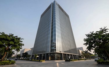 Professional photography of a sleek, modern commercial glass skyscraper in Noida’s business district. The shot is a low-angle perspective showing the building reaching into a clear sky. South Asian / Indian corporate environment with clean pavement and manicured trees, reflecting a sophisticated and expert business atmosphere.