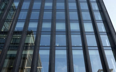 A low-angle architectural photograph of a modern glass office building facade reflecting a clear sky. The image features deep slate blue glass and dark charcoal steel frames, conveying a sense of legal authority and corporate stability.