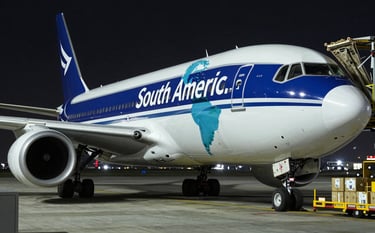 A modern cargo airplane being loaded with packages at night under bright industrial lights, reflecting Deep Navy Blue and Pale Greyish Blue colors, symbolizing speed to South America.