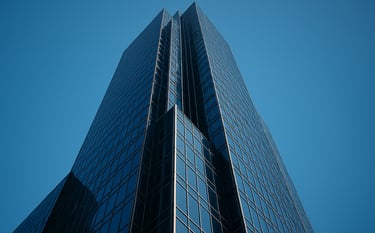 A low-angle exterior shot of a majestic glass-and-steel skyscraper in a North American financial district, reflecting the clear blue sky. The composition is powerful and secure, using a palette of dark blue and polished silver.