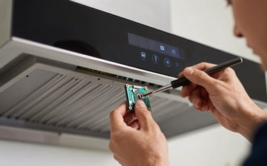 A technician using precision tools to repair the electronic touch panel of a high-end kitchen chimney. The scene is shot with a shallow depth of field, emphasizing the technical expertise and reliability.