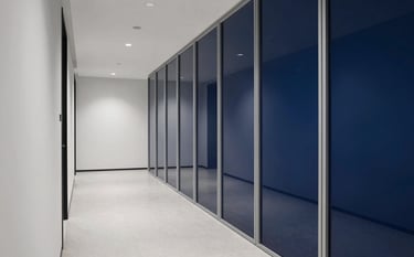 Wide shot of a modern, minimalist law firm corridor with mist white walls and midnight blue glass partitions, reflecting a sense of order and authority.
