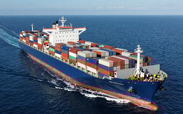 A professional aerial photograph of a massive cargo ship loaded with hundreds of containers navigating through the deep blue waters of a North American coastal route. The lighting is bright and clear, emphasizing modern industrial power and logistics precision.