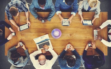 Overhead view of a diverse business team analyzing data on digital tablets and laptops around a wooden table.