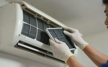 A close-up photograph of a technician's hands wearing gloves while carefully cleaning the filters of an indoor AC unit. The lighting is soft and professional, highlighting the attention to detail in a clean Latin American household setting.
