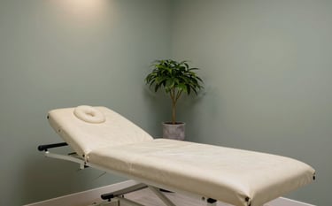 A professional and clean interior of a chiropractor clinic. A soft parchment treatment table sits in a room with muted sage walls. A small plant in a stone grey pot adds a touch of organic life. High-end, strategic atmosphere with soft, overhead lighting.