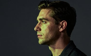 A visually powerful studio portrait of a modern professional. Dramatic lighting with vibrant lime green accents hitting the subject's profile against a deep charcoal backdrop. Impactful and credible aesthetic.