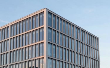 A minimalist and sharp architectural shot of a modern glass office building at sunset. The pale off-white facade reflects hints of a royal blue evening sky. Clean, professional corporate photography.